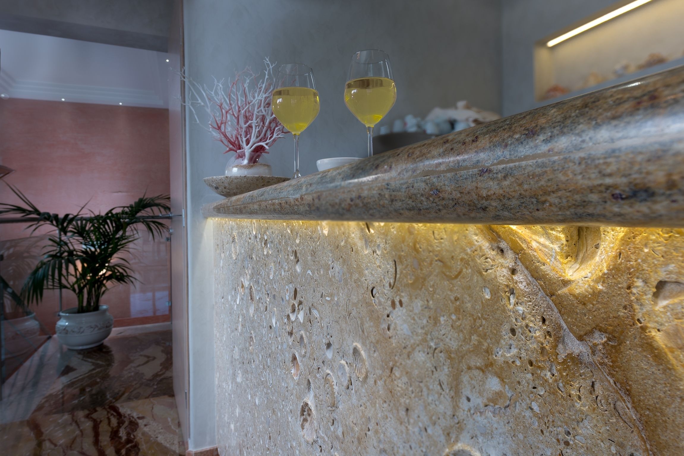 A marble reception desk with two glasses of white wine, a potted plant, and a vase with red branches.