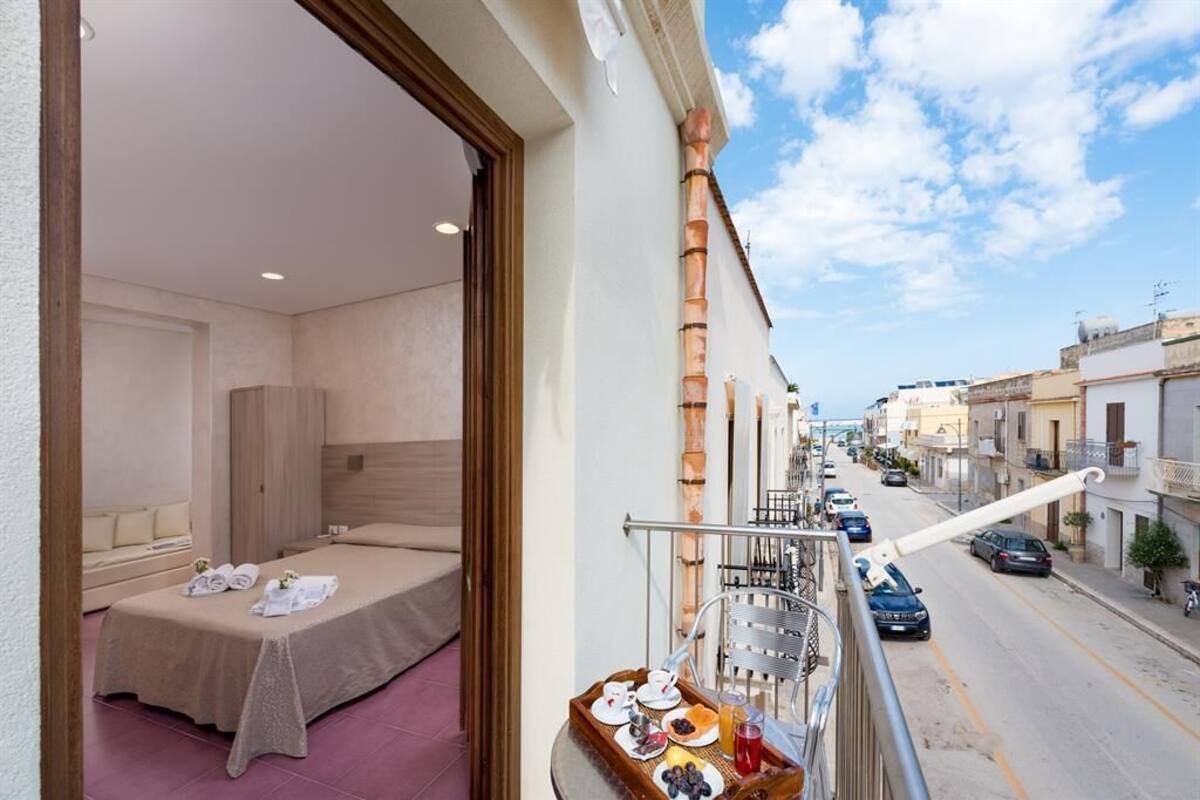 Une chambre d’hôtel avec un balcon, un lit et un plateau de petit-déjeuner comprenant des assiettes, des tasses et un panier de fruits.