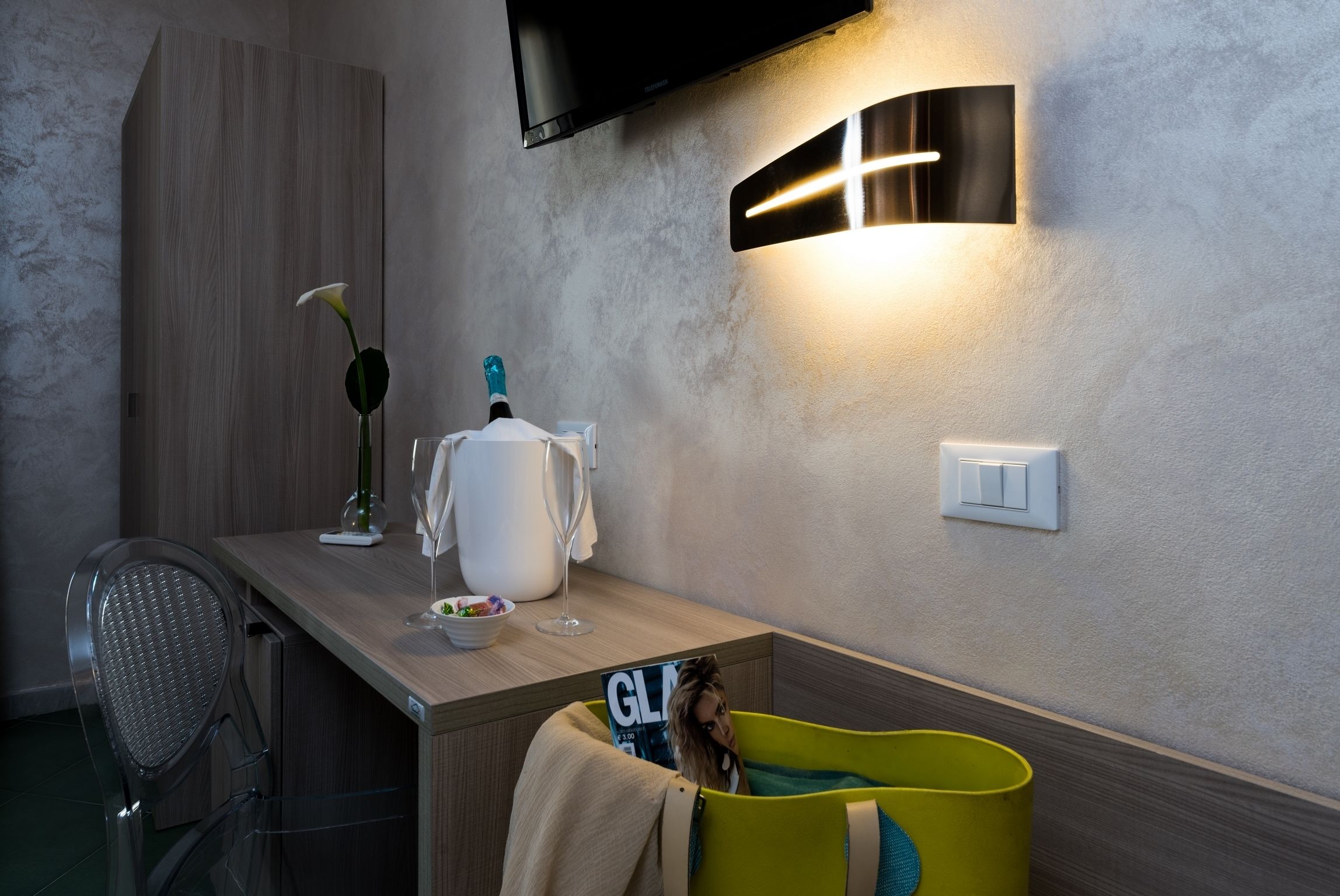 A modern kitchen with a wooden countertop, a built-in TV, a wall-mounted light, and a green trash bin.