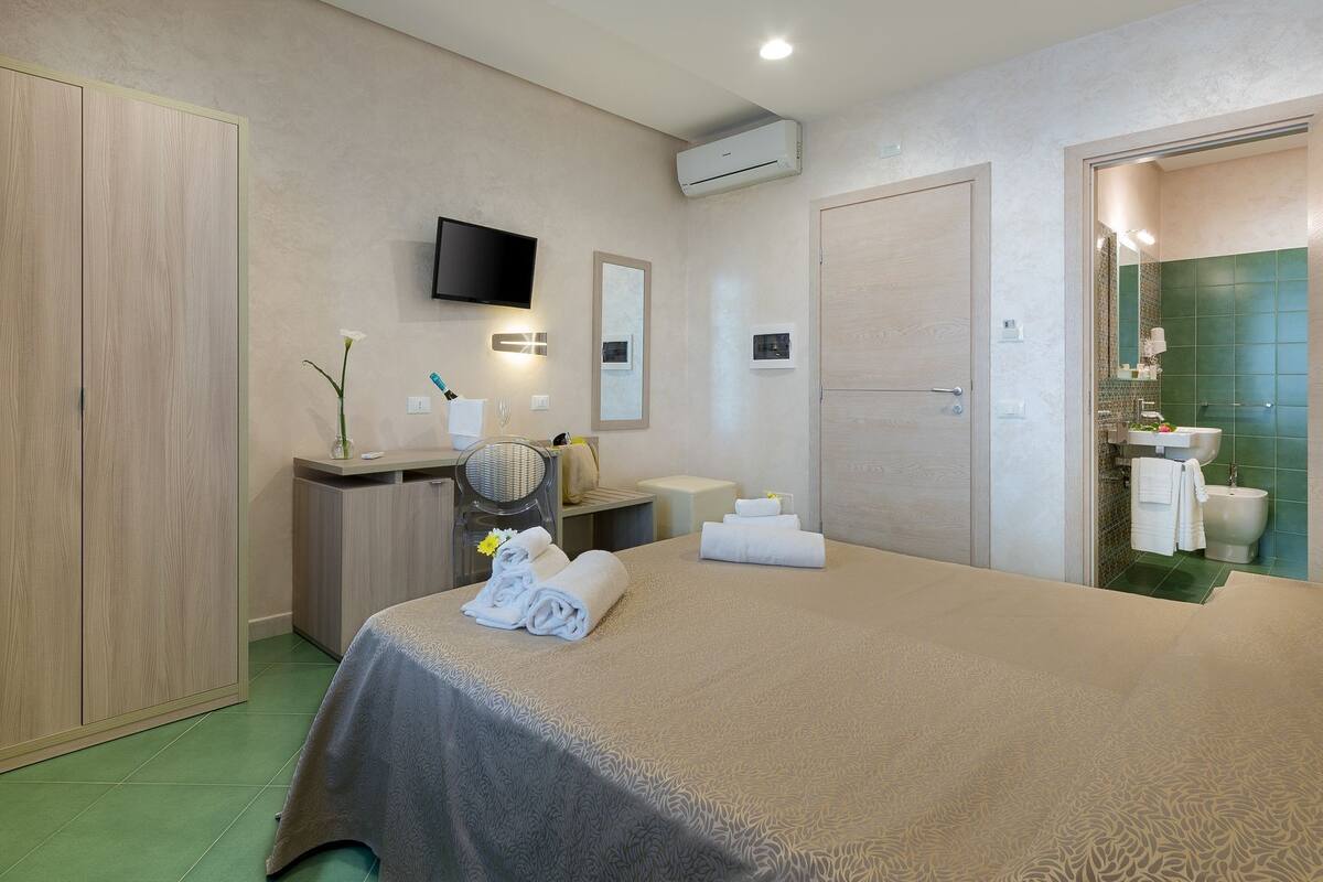Une chambre d’hôtel avec un lit, un bureau, une télévision et une salle de bain visible à travers une porte ouverte.