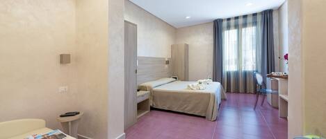 A hotel room with a bed, a desk, a chair, a small table, and a magazine on the bed.