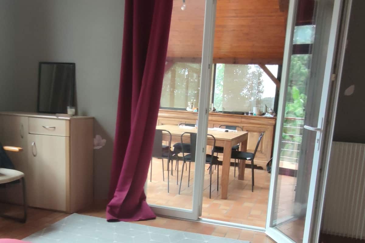 Une chambre avec un lit, un bureau et une chaise. Une porte-fenêtre coulissante donne sur un balcon équipé d’une table et de chaises.