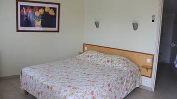 Une chambre à coucher avec une couvre-lit à motifs floraux, une tête de lit en bois, une table de chevet et un tableau encadré au mur.