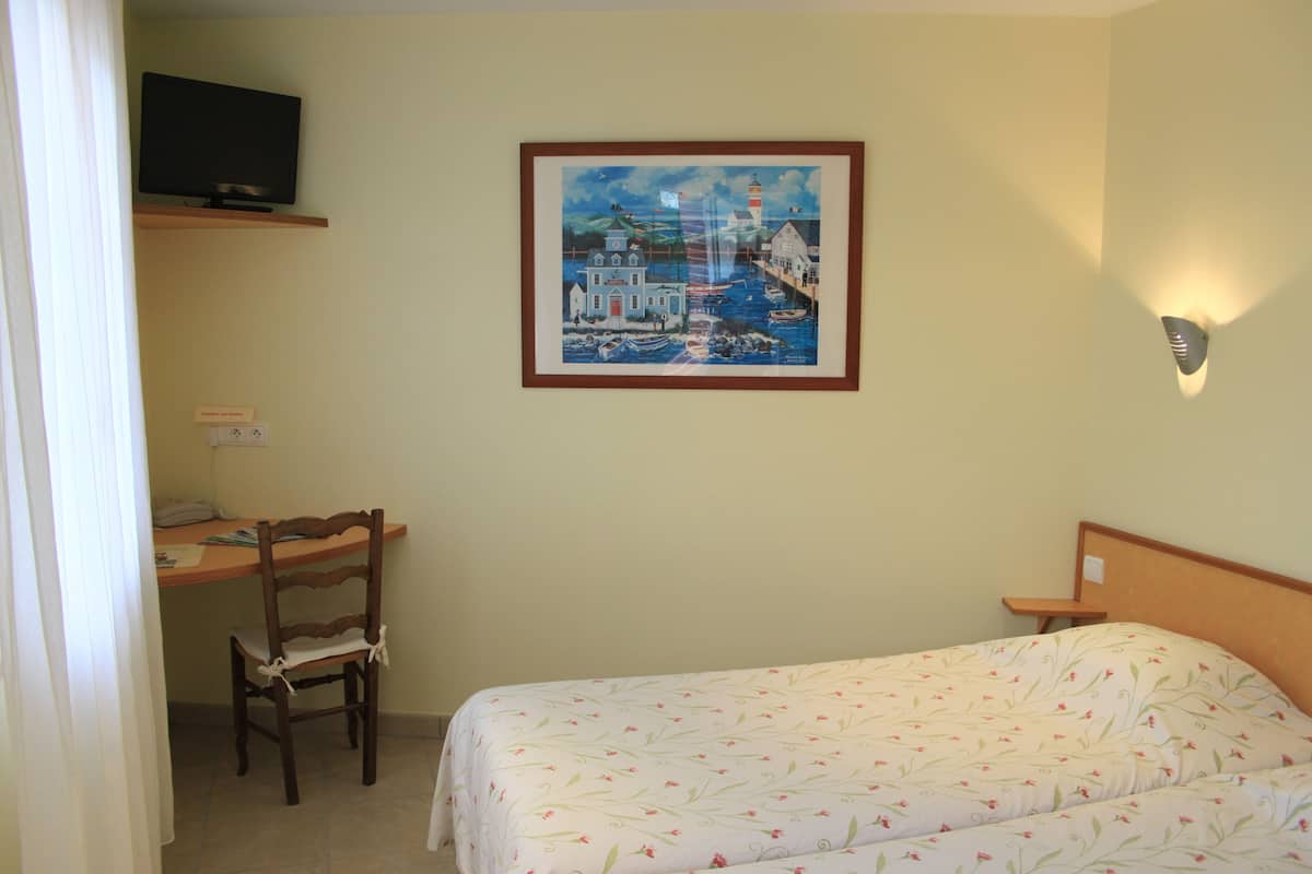 Une chambre d’hôtel avec un lit, un bureau et une chaise, un téléviseur posé sur une étagère et un tableau accroché au mur.