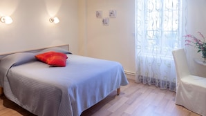 Een slaapkamer met een bed, een stoel, een raam met dunne gordijnen en wandlampen.