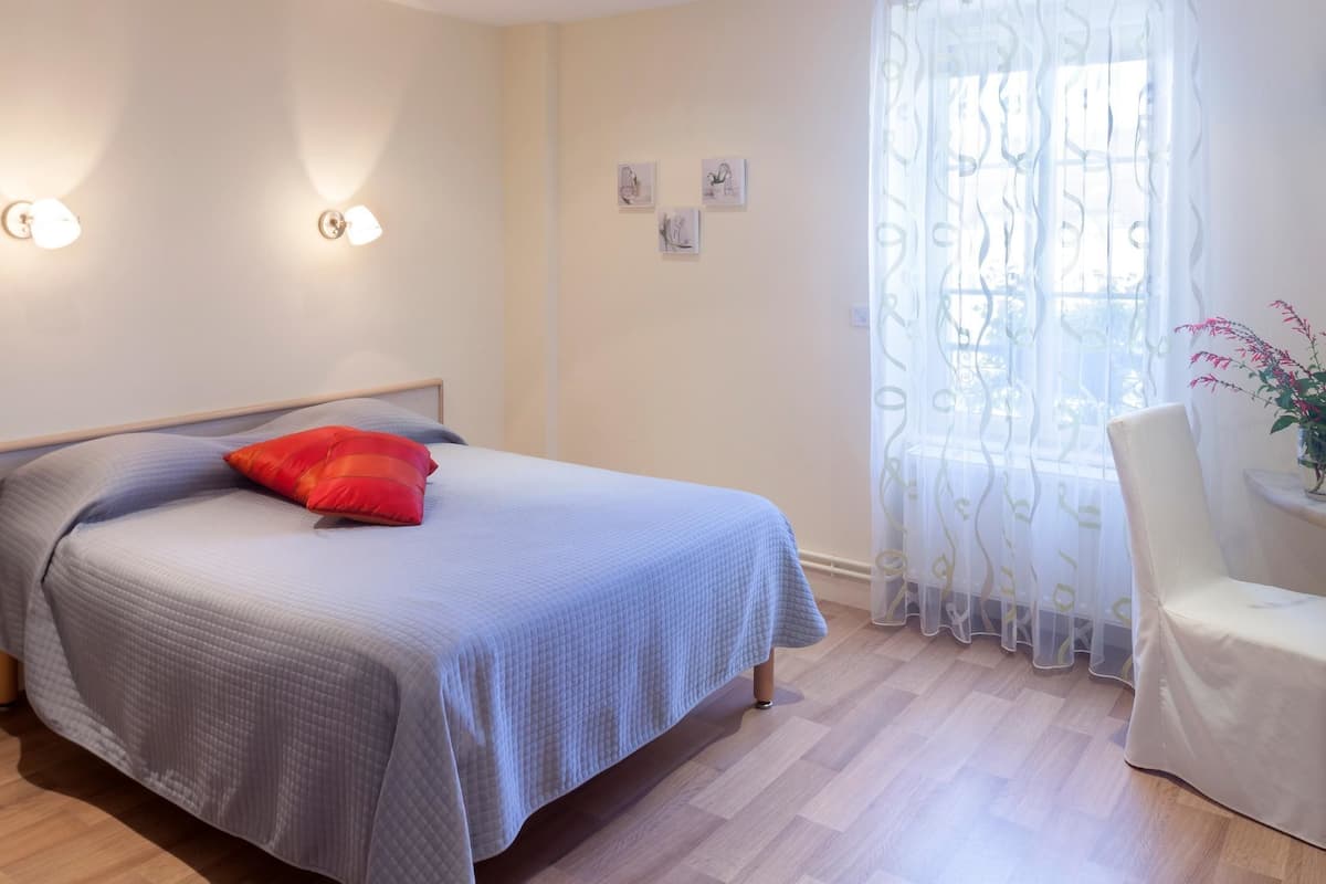 Une chambre à coucher avec un lit, une chaise, une fenêtre avec des rideaux légers et des lampes fixées au mur.