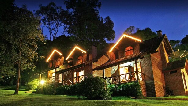 A large, multi-story house with a prominent brick facade, multiple windows, and a well-lit exterior. - Chalets do Vale (Gramado)