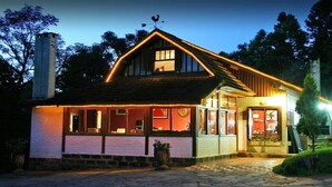 A two-story house with a sloped roof, a chimney, and a porch with a railing. - Chalets do Vale (Gramado)