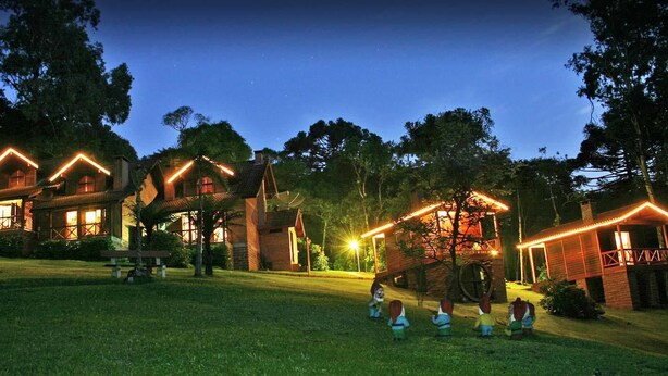 A rustic lodge with multiple wooden cabins, each featuring a distinctively shaped roof and illuminated by warm lights. - Chalets do Vale (Gramado)