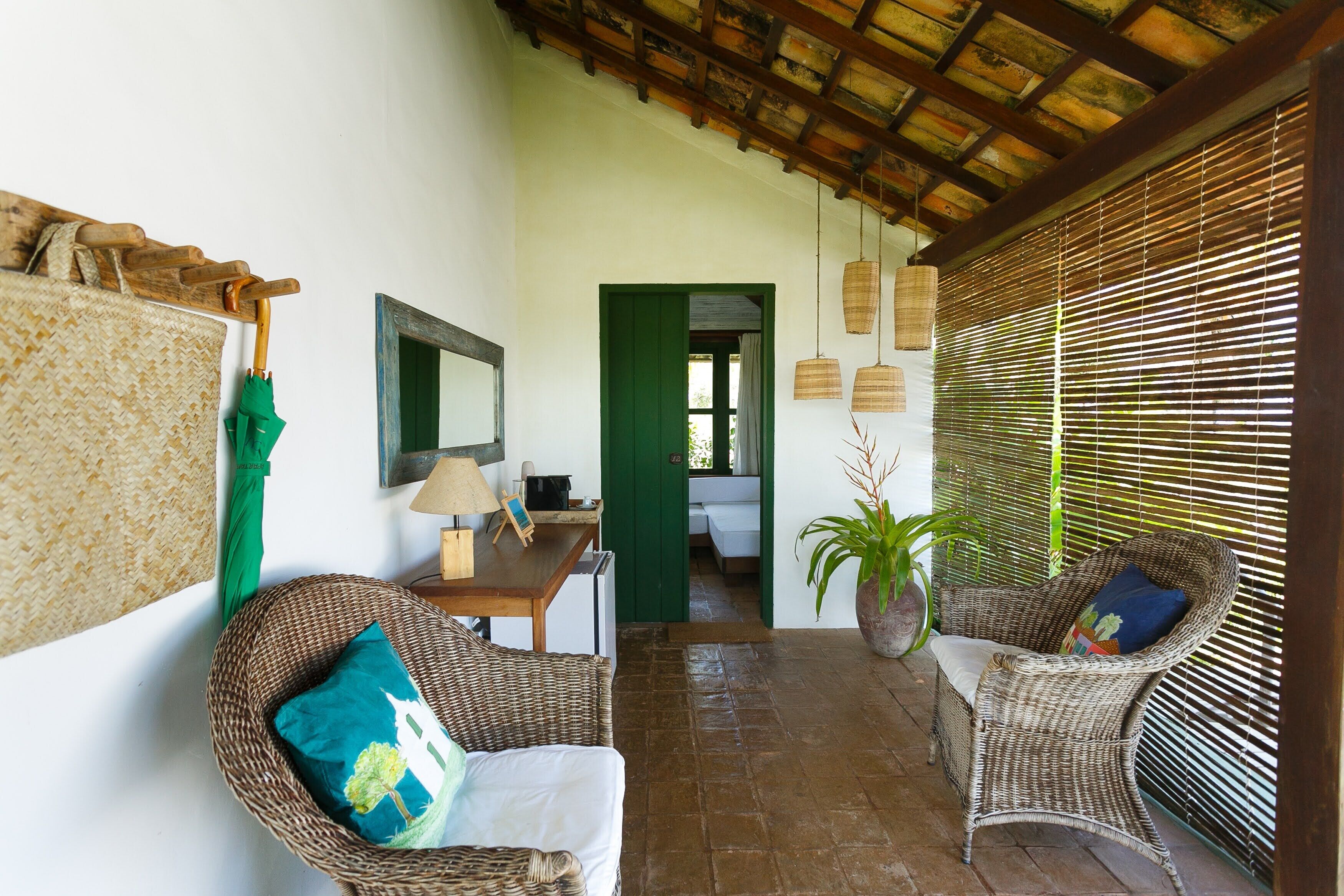 Une pièce meublée de mobilier en osier, avec une porte verte et un plafond orné de poutres en bois.