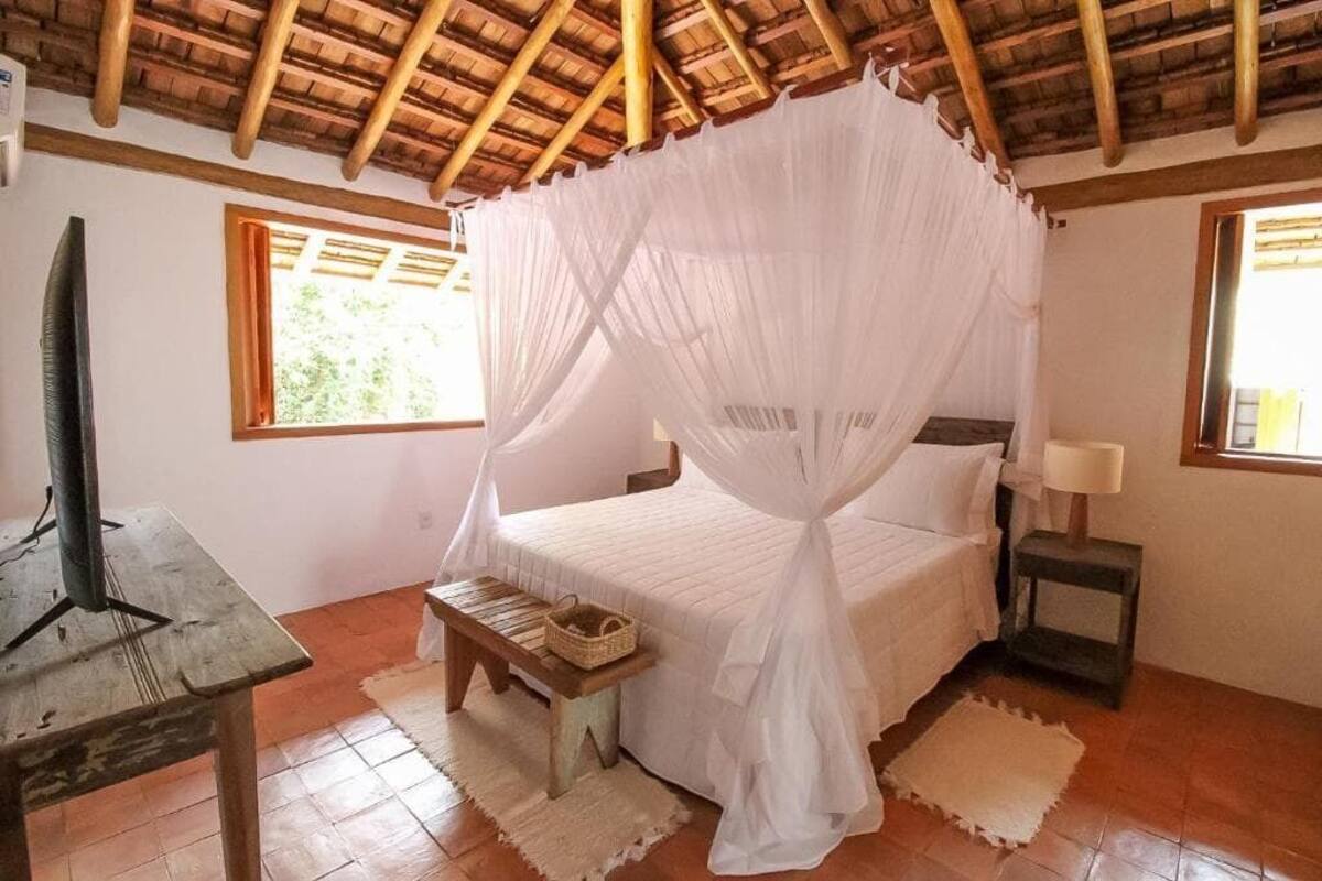 A bedroom with a bed under a canopy, a bedside table with a lamp, and a window with curtains.