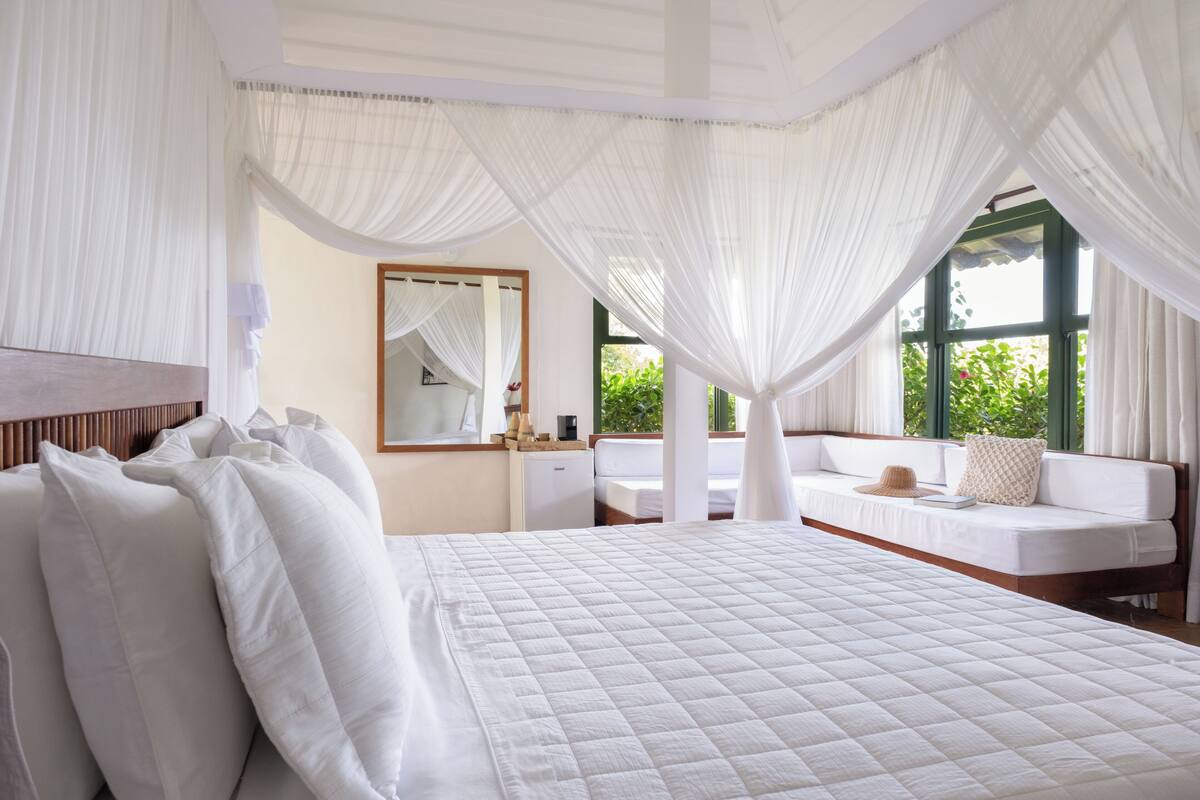 A bedroom with a large bed, a nightstand, a desk, and a window with curtains.