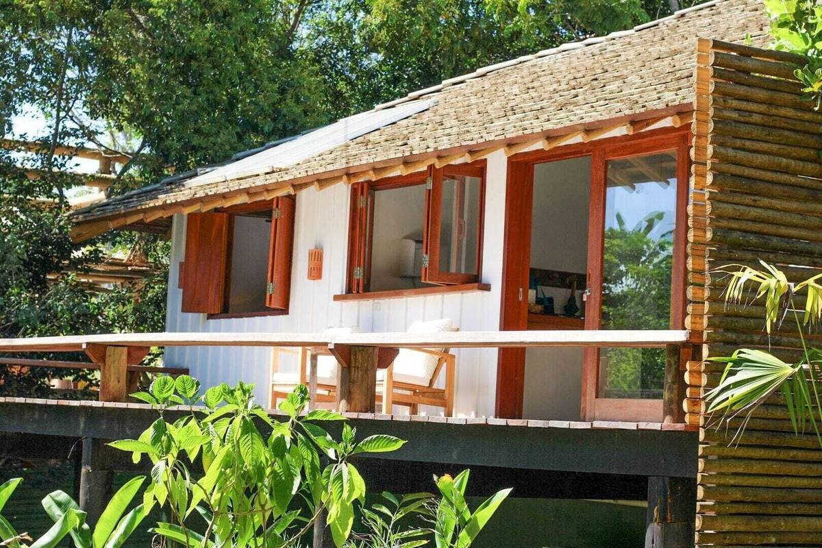 A wooden house with large windows and a balcony, surrounded by greenery.