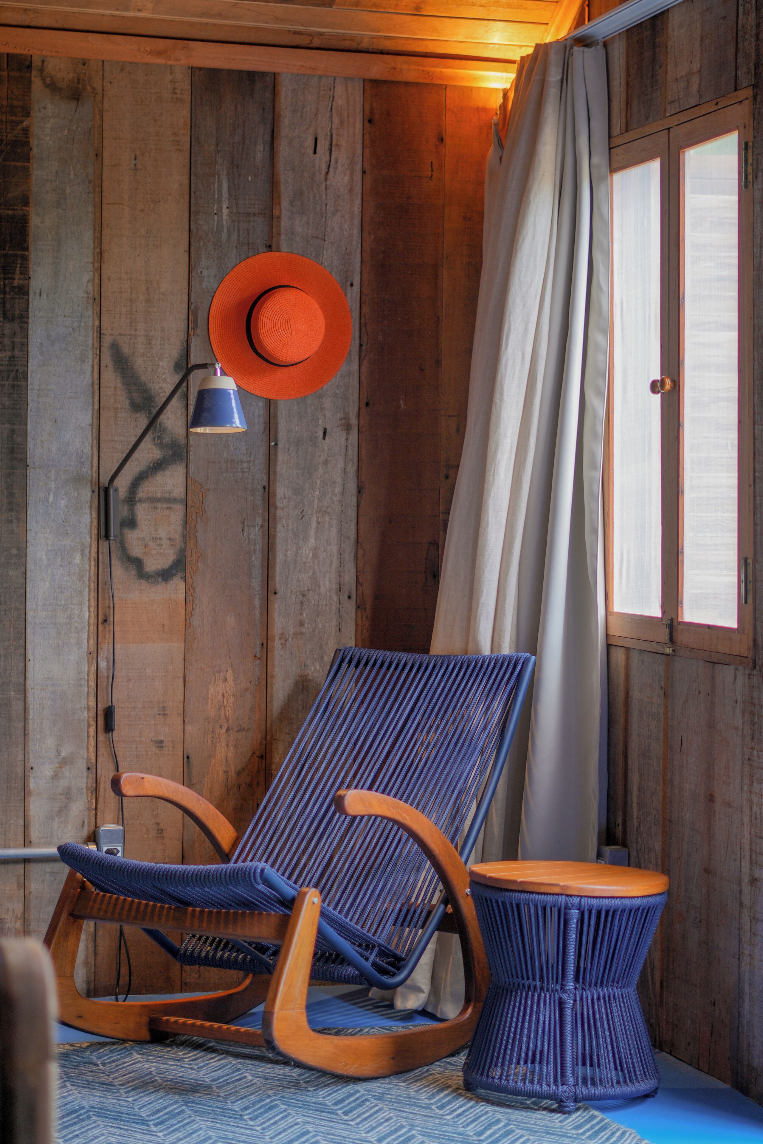 Una habitación de madera con una mecedora, una mesita y una lámpara.