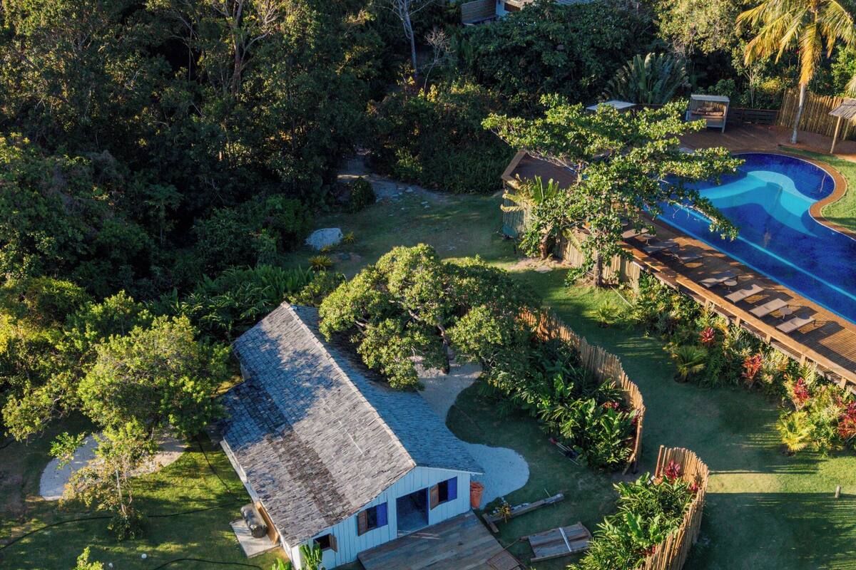 A large, private estate with a swimming pool, surrounded by dense tropical vegetation and multiple buildings.