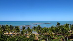 A tropical beach resort with palm trees, a sandy beach, and a clear blue sea. - Pousada Outeiro (Porto Seguro)