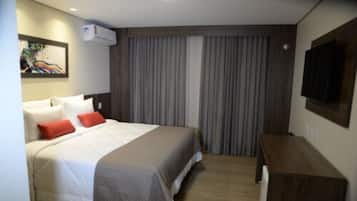 Quarto de hotel com cama, escrivaninha, televisão e um quadro na parede.