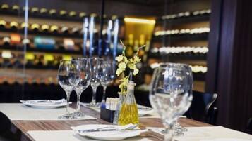A restaurant setting with a long table set for dining, featuring wine glasses, plates, and a small vase with flowers.