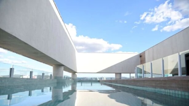 Un bâtiment moderne doté d’une grande piscine extérieure et surplombant un ciel d’un bleu éclatant.