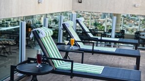 Un espace de détente sur le toit, avec des fauteuils et des tables à rayures, une balustrade en verre et une vue sur la ville.