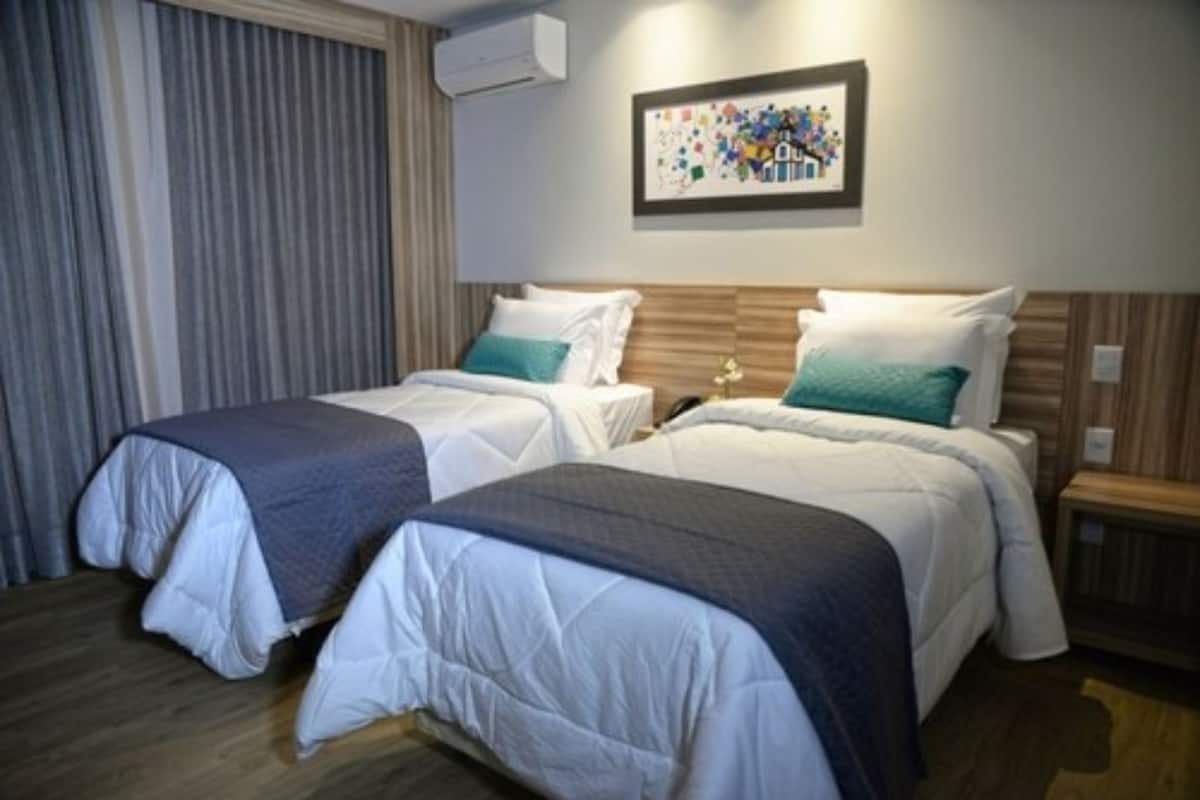 Habitación de hotel con dos camas, un cabecero de madera, una obra de arte enmarcada en la pared y una ventana con cortinas.