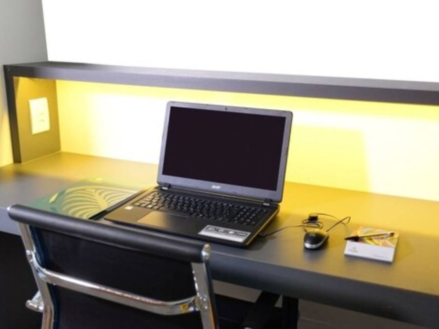 Una computadora portátil sobre un escritorio, con una silla al frente.