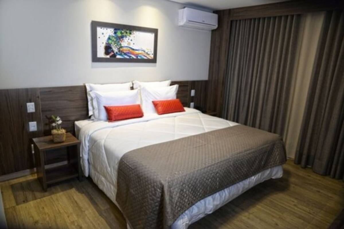 Habitación de hotel con cama, mesita de noche, aire acondicionado en la pared y ventana con cortinas.