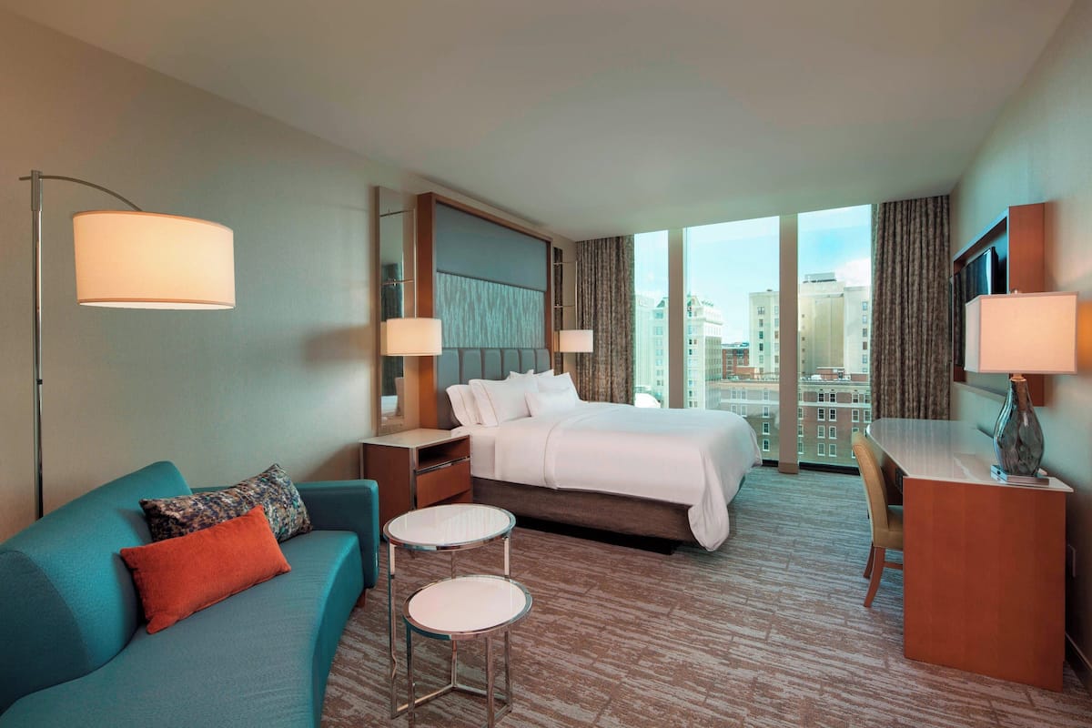 A hotel room with a bed, a sofa, a desk, and a view of the city.