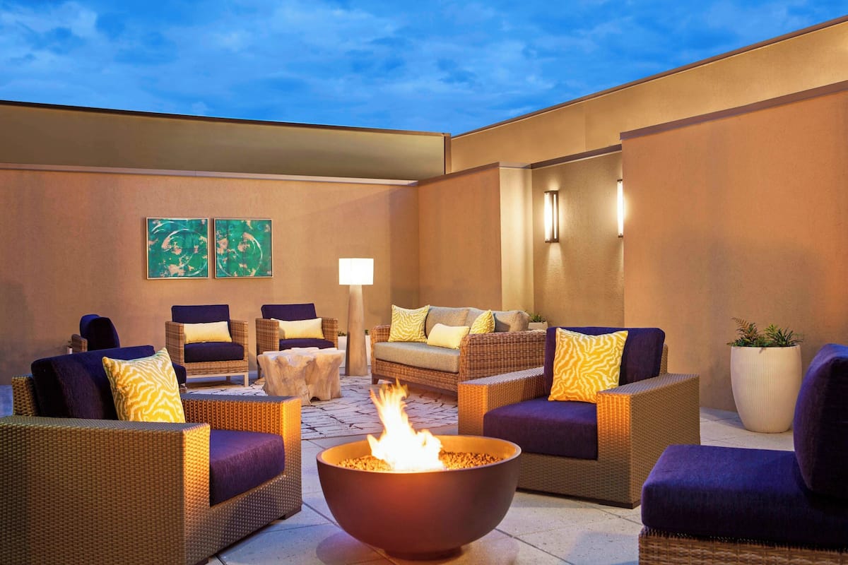 An outdoor seating area with wicker furniture, a central fire feature, and wall-mounted lighting.