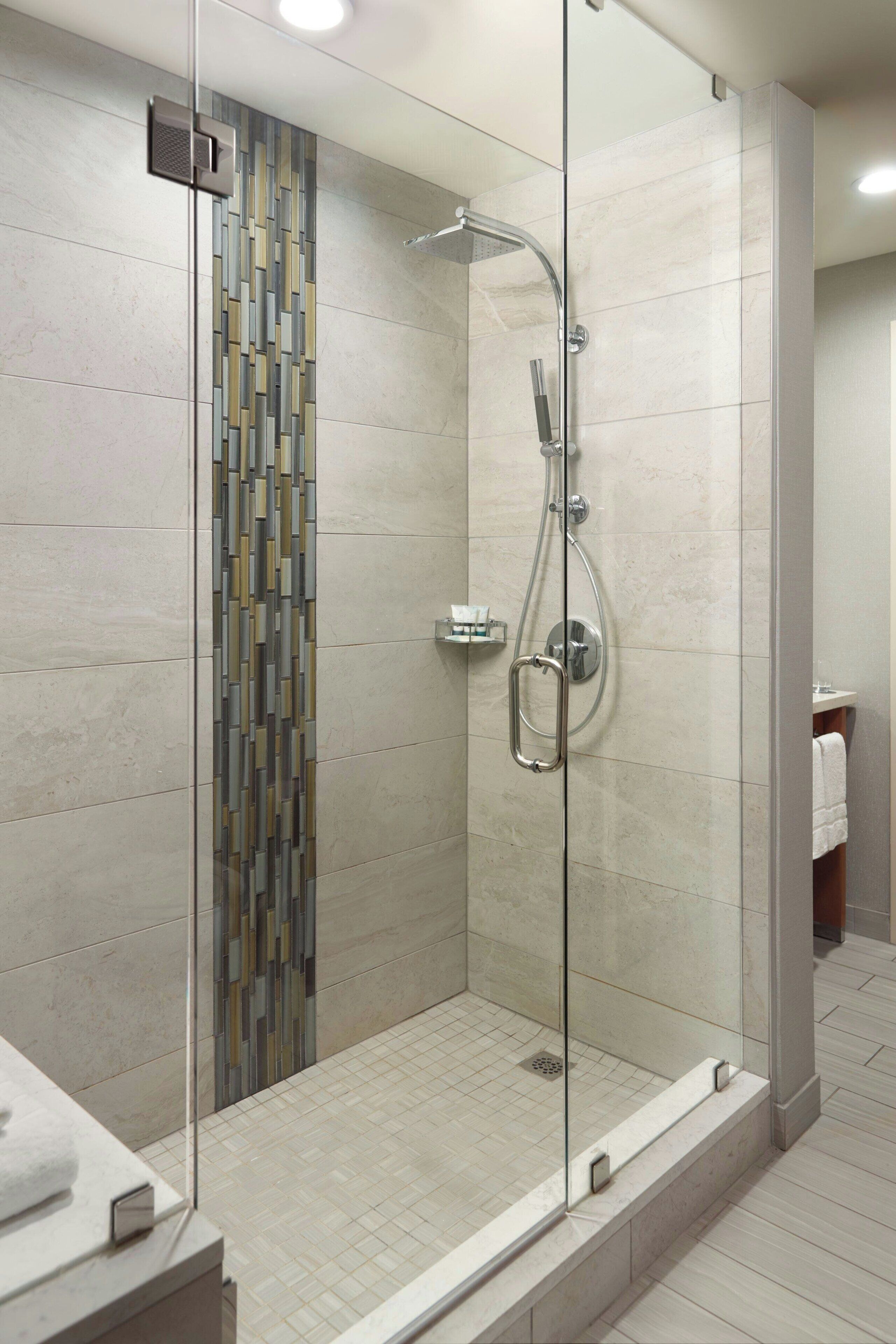 A modern shower with a glass door, a tiled wall with a geometric pattern, and a visible bathroom counter with a towel.