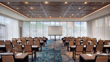 A conference room with a large screen, multiple tables with chairs, and a patterned carpet.