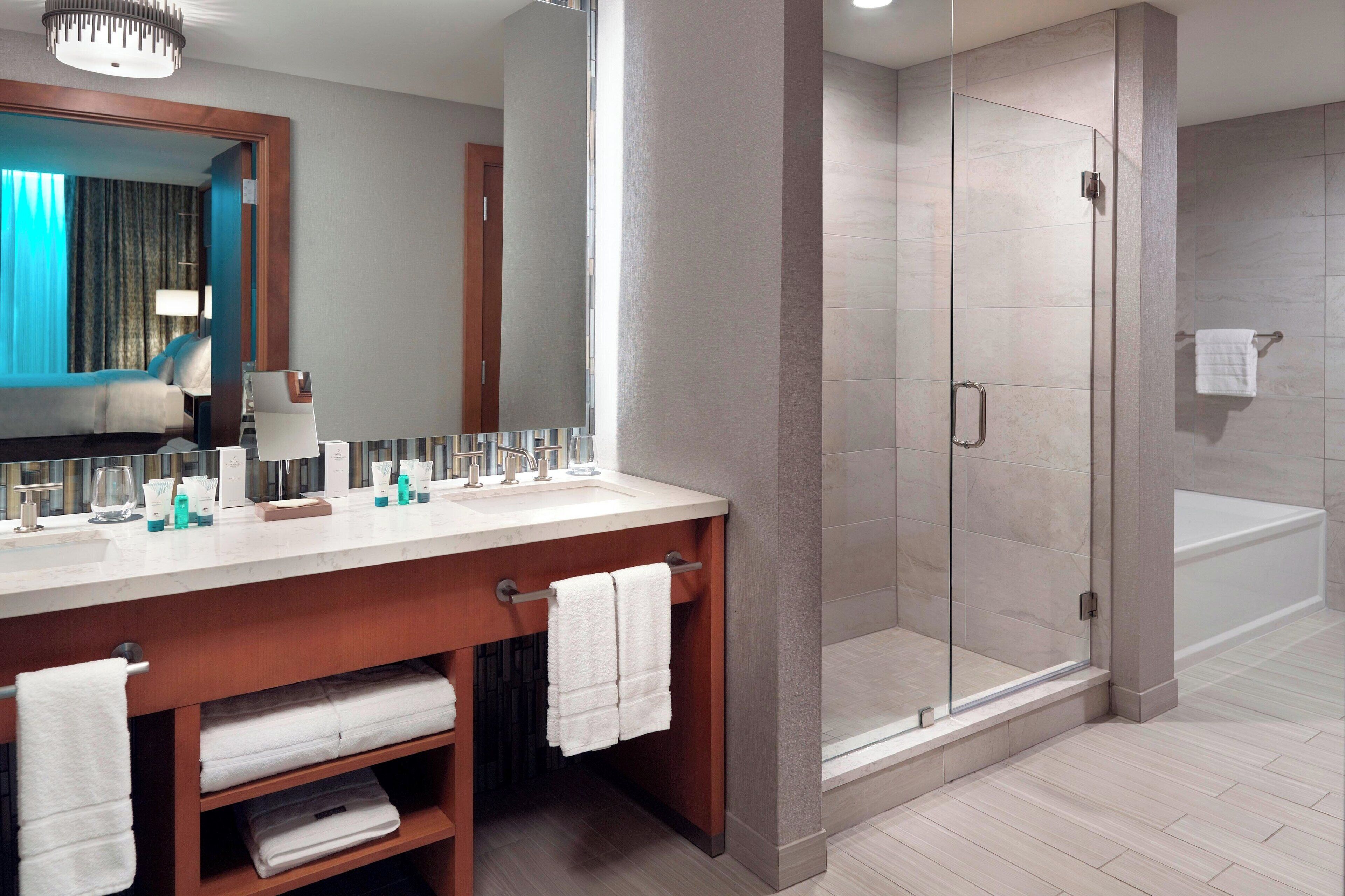 A modern bathroom with a large mirror, dual sinks, and a glass-enclosed shower.