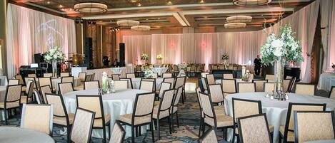 Een balzaal met ronde tafels, stoelen en bloemstukken als decoratie.