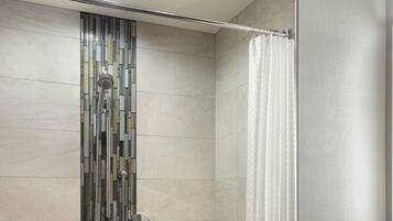 A modern bathroom with a shower, a wooden bench, a towel rack, and a mirror.