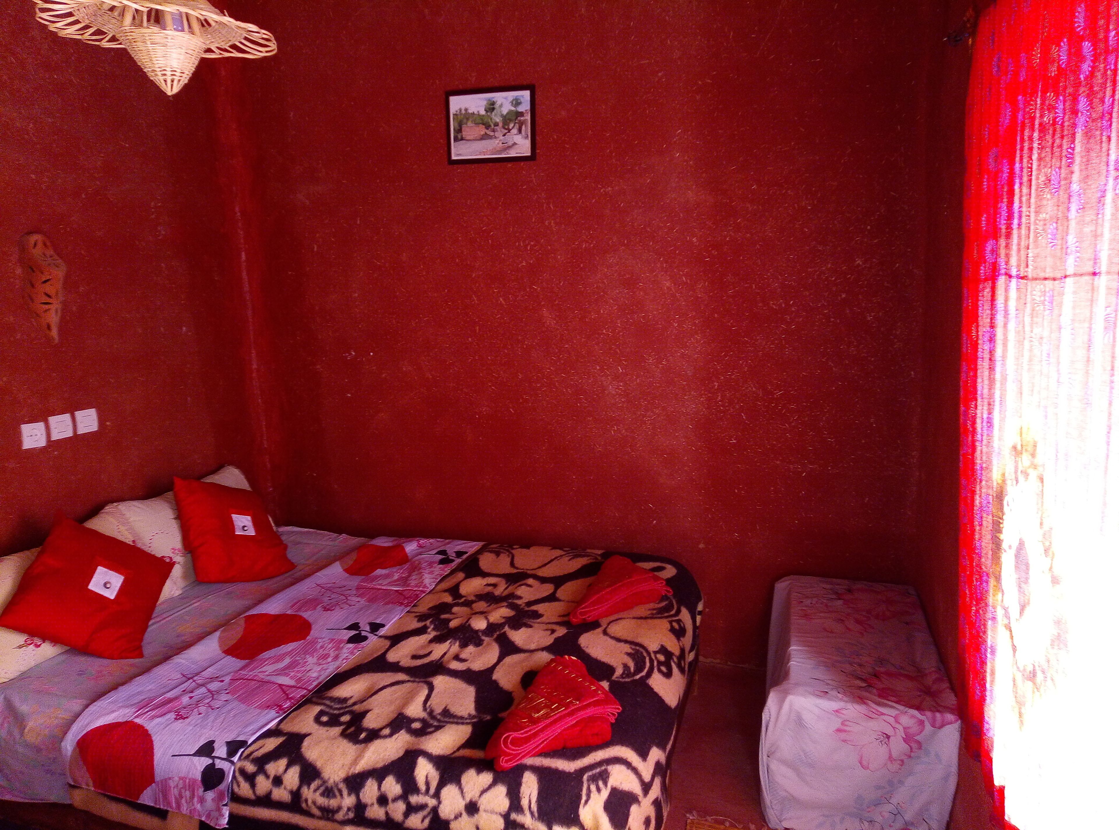 A small, red-walled room with a single bed, a small table, and a picture on the wall.