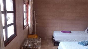 Una habitación pequeña y rústica con dos camas, un banco de madera y una ventana con cortinas.