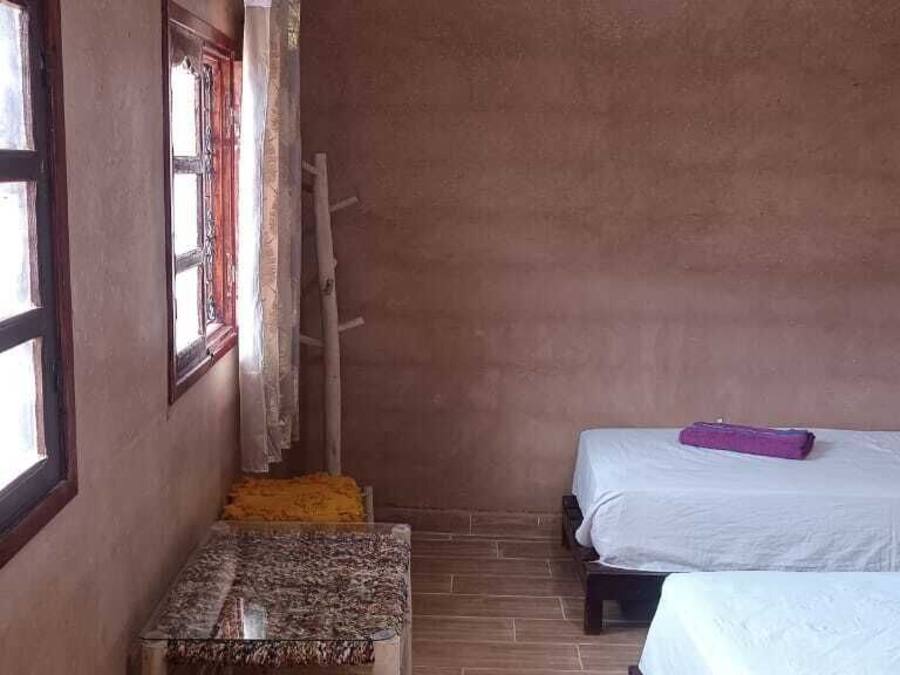 Una habitación pequeña y rústica con dos camas, un banco de madera y una ventana con cortinas.