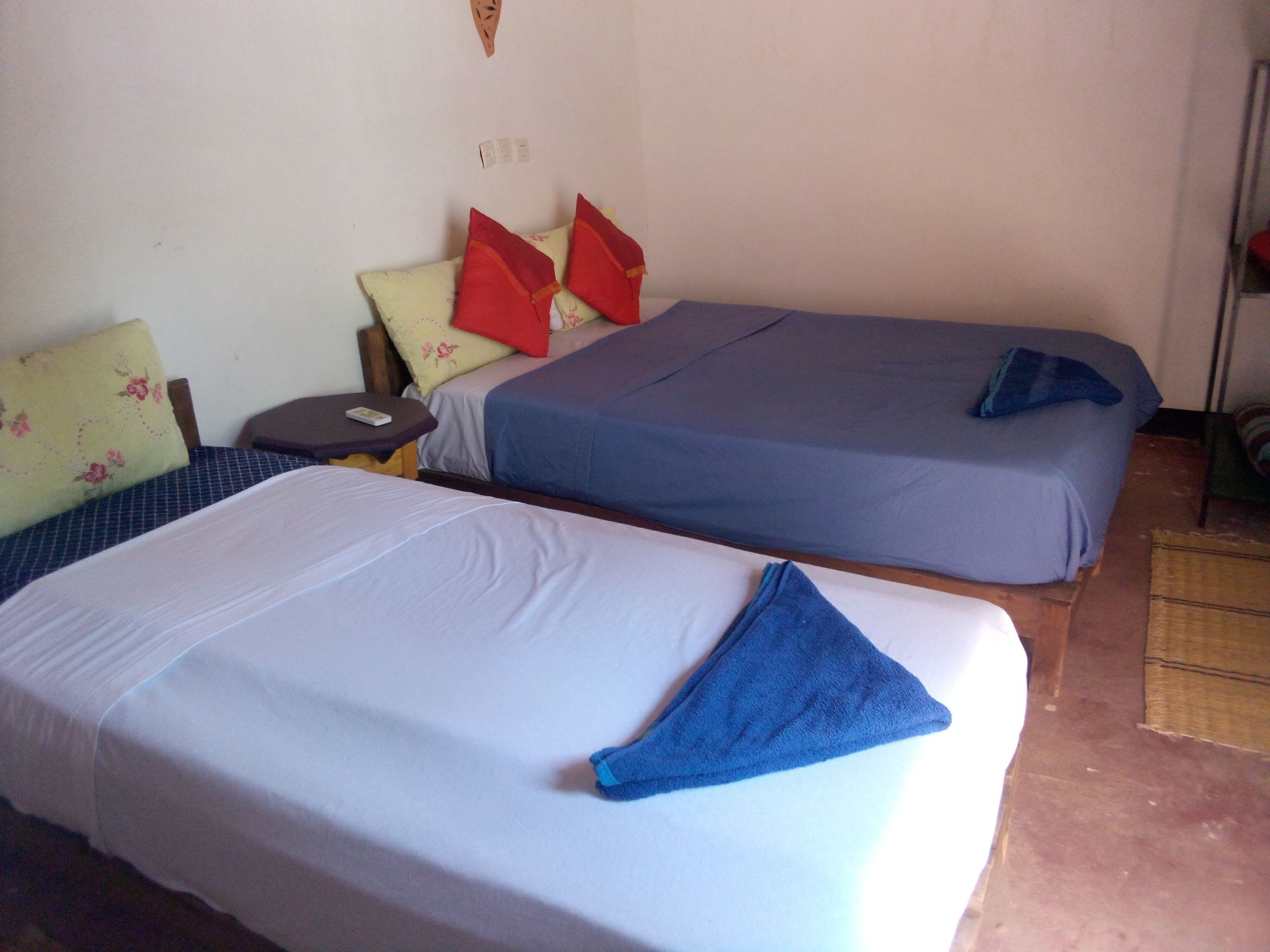 A room with two beds, each with a different colored bedspread. There are pillows on the beds, and a small table with a remote control on it.