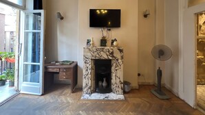 A room with a fireplace, a television mounted above it, a desk with drawers, and a fan. - Sufi House (Cairo)