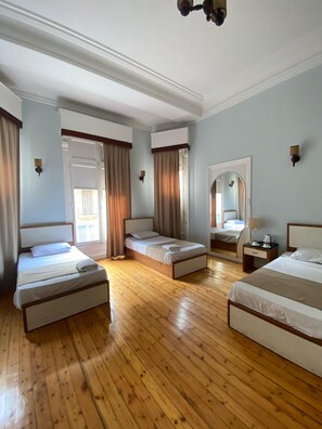 Een hotelkamer met drie bedden, houten vloeren en een grote spiegel.
