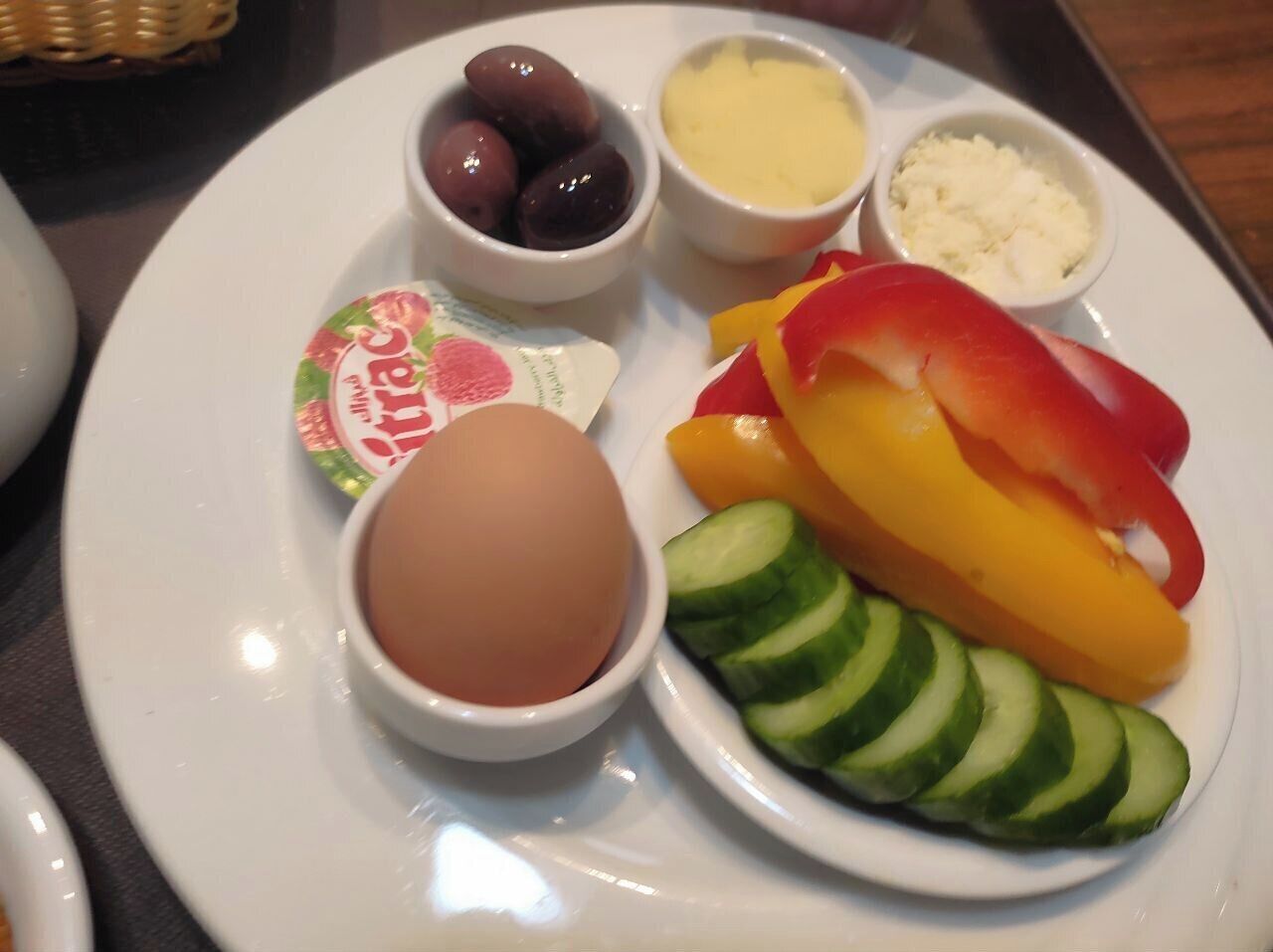 Un plato con rodajas de pepino, pimientos, un huevo duro, aceitunas, queso y yogur.