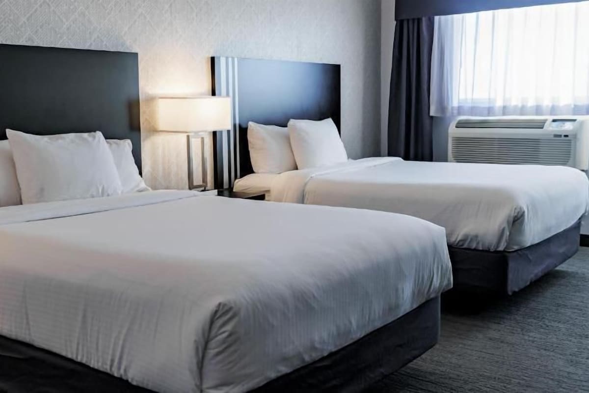 A hotel room with two beds, a nightstand with a lamp, and an air conditioning unit.