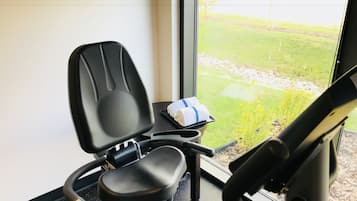 Un gimnasio con equipo de ejercicio, una ventana que ofrece vistas a un espacio verde y una pequeña mesa con toallas.