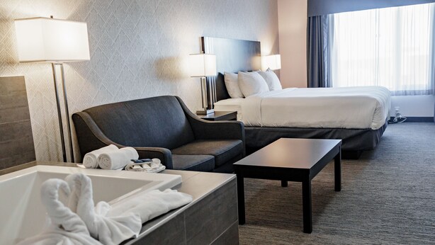A hotel room with a bed, a sofa, a desk, a lamp, and a bathtub with towels. - Park Inn by Radisson Edmonton Airport (Leduc)