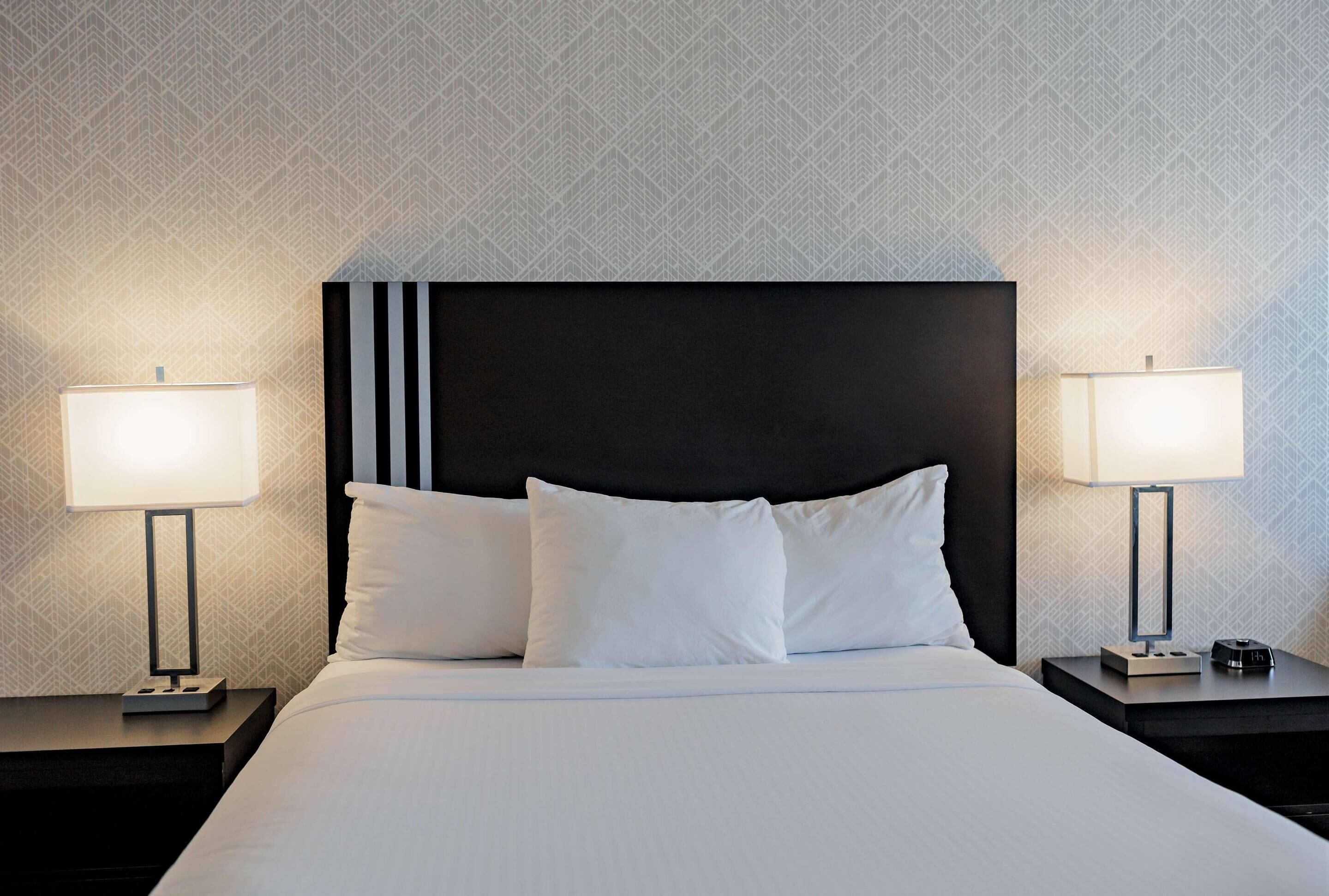 A hotel room with a large bed, two bedside tables, and two wall-mounted lamps.