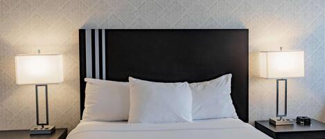 Una habitación de hotel con una cama grande, dos mesitas de noche y dos lámparas de pared.