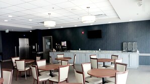 A modern dining area with round tables and chairs, a coffee station, and a flat-screen TV on the wall. - Park Inn by Radisson Edmonton Airport (Leduc)