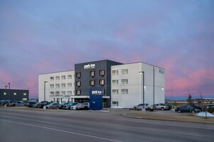 Um hotel de vários andares com a placa 'Park Inn', estacionamento e céu claro.