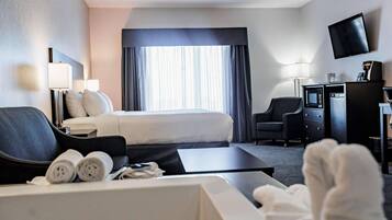 Quarto de hotel com cama, escrivaninha, televisão e móvel de televisão com micro-ondas.