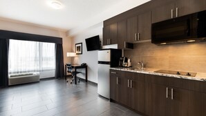 A modern kitchen with dark wood cabinets, a built-in microwave, and a large window with curtains. - Park Inn by Radisson Edmonton Airport (Leduc)